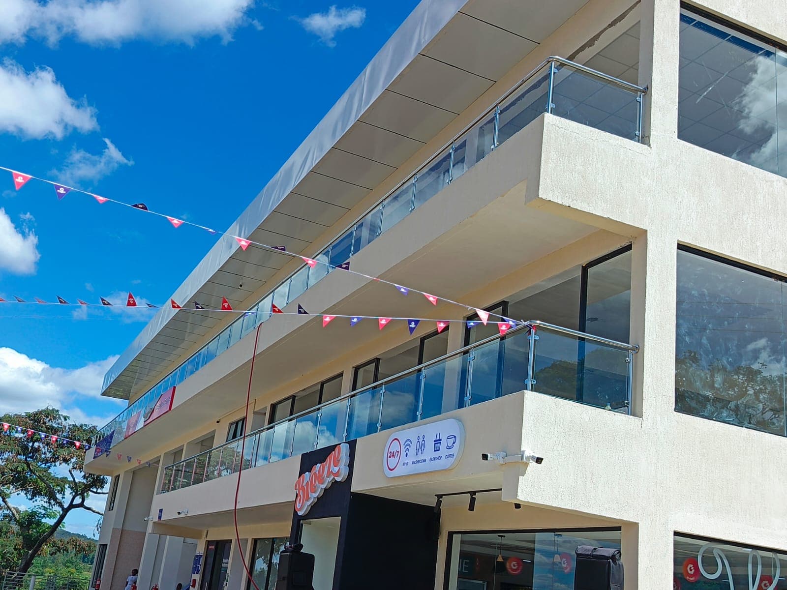 Completed elevation — handover-ready three-storey service hub with glass balconies, convenience retail branding, and finished hard landscaping.